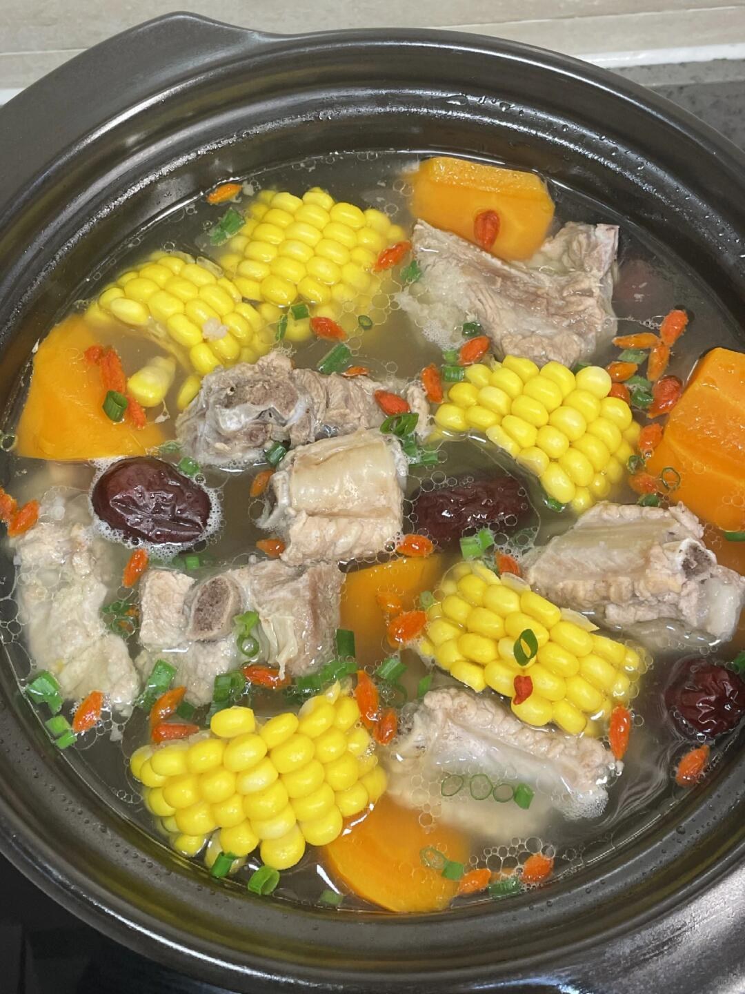Corn rounds, pork ribs, carrot chunks and red dates in a black clay pot of clear soup.