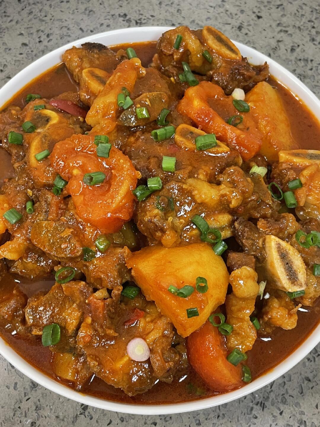 Beef rib pieces and potatoes in a tomato sauce topped with chopped scallions.