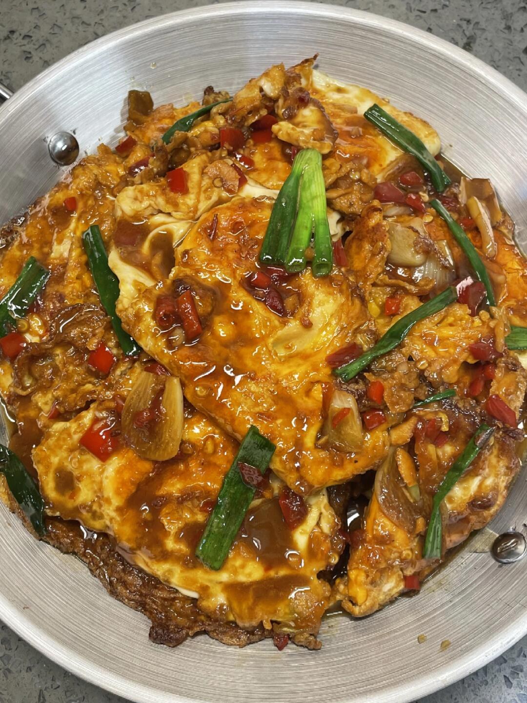 Fried eggs with browned edges, green scallions and red peppers on a pale plate.