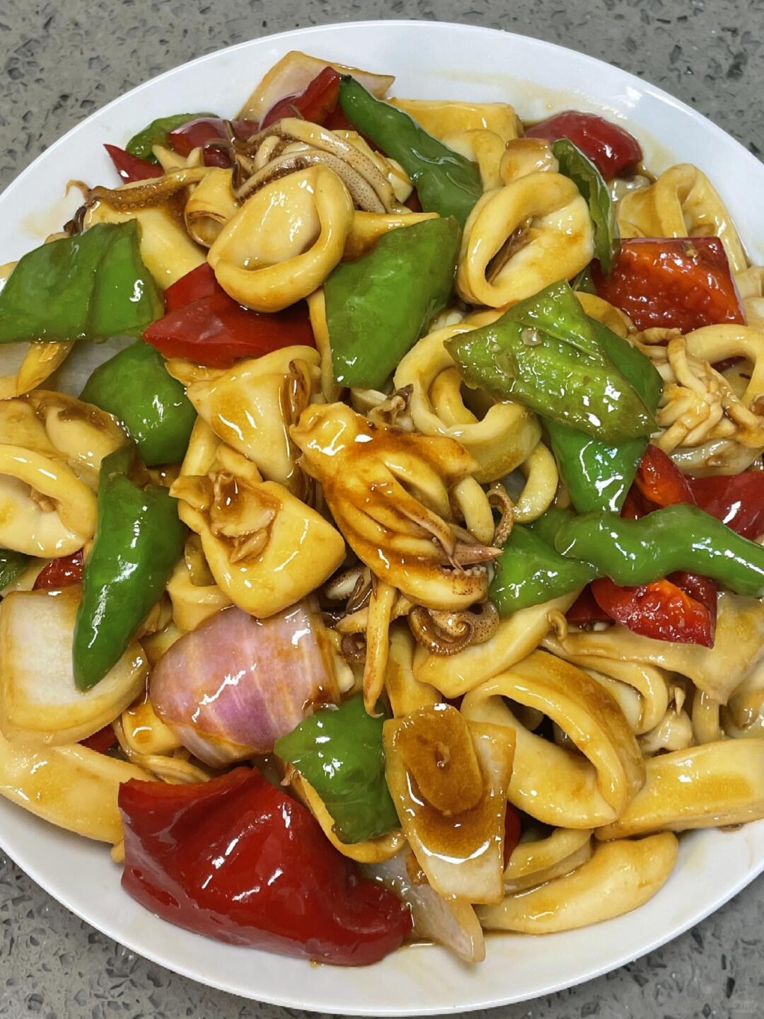 Pale squid rings with green and red peppers and purple onion on a white plate.