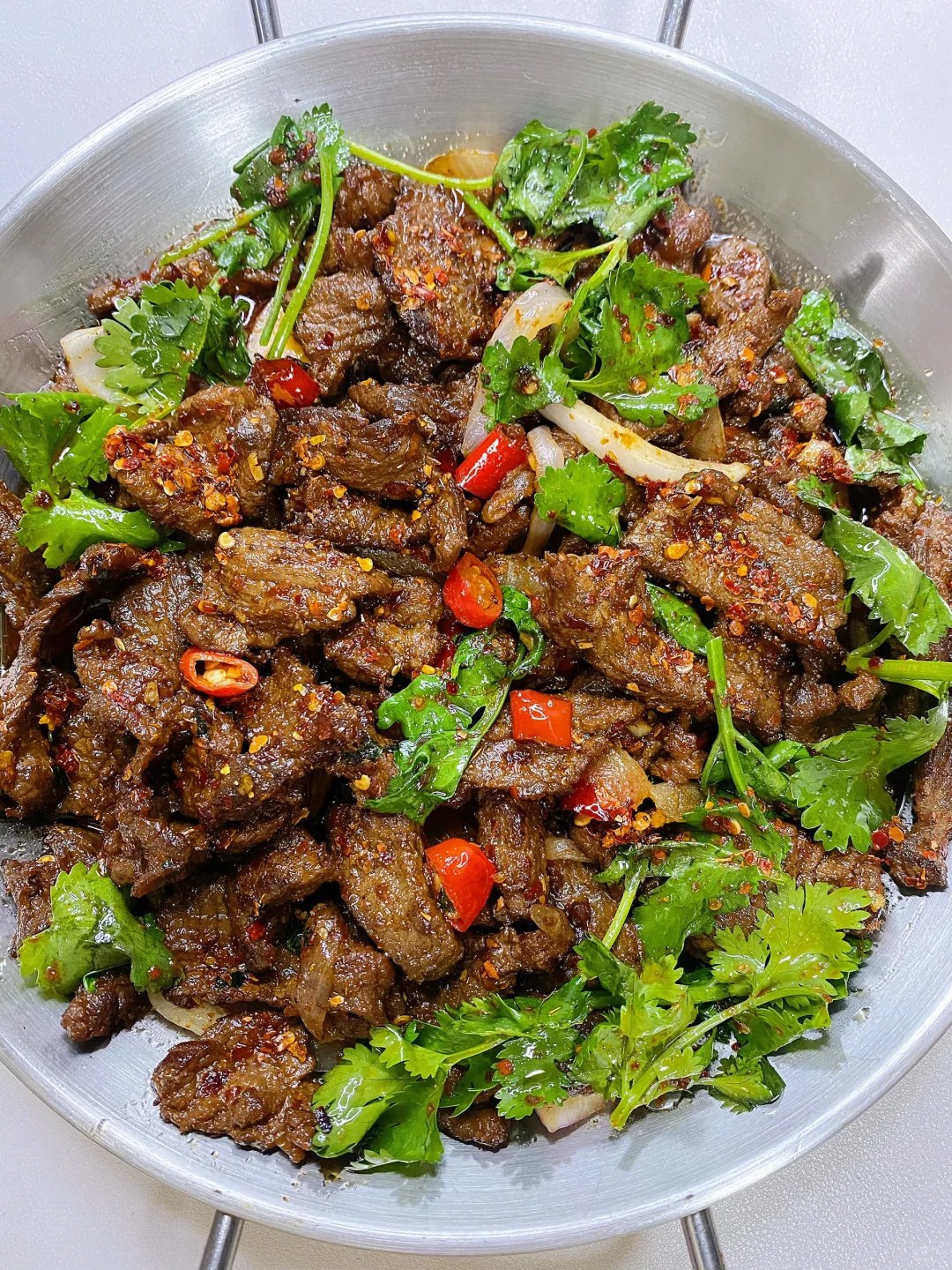 Brown beef slices with red chiles, onion and green cilantro.