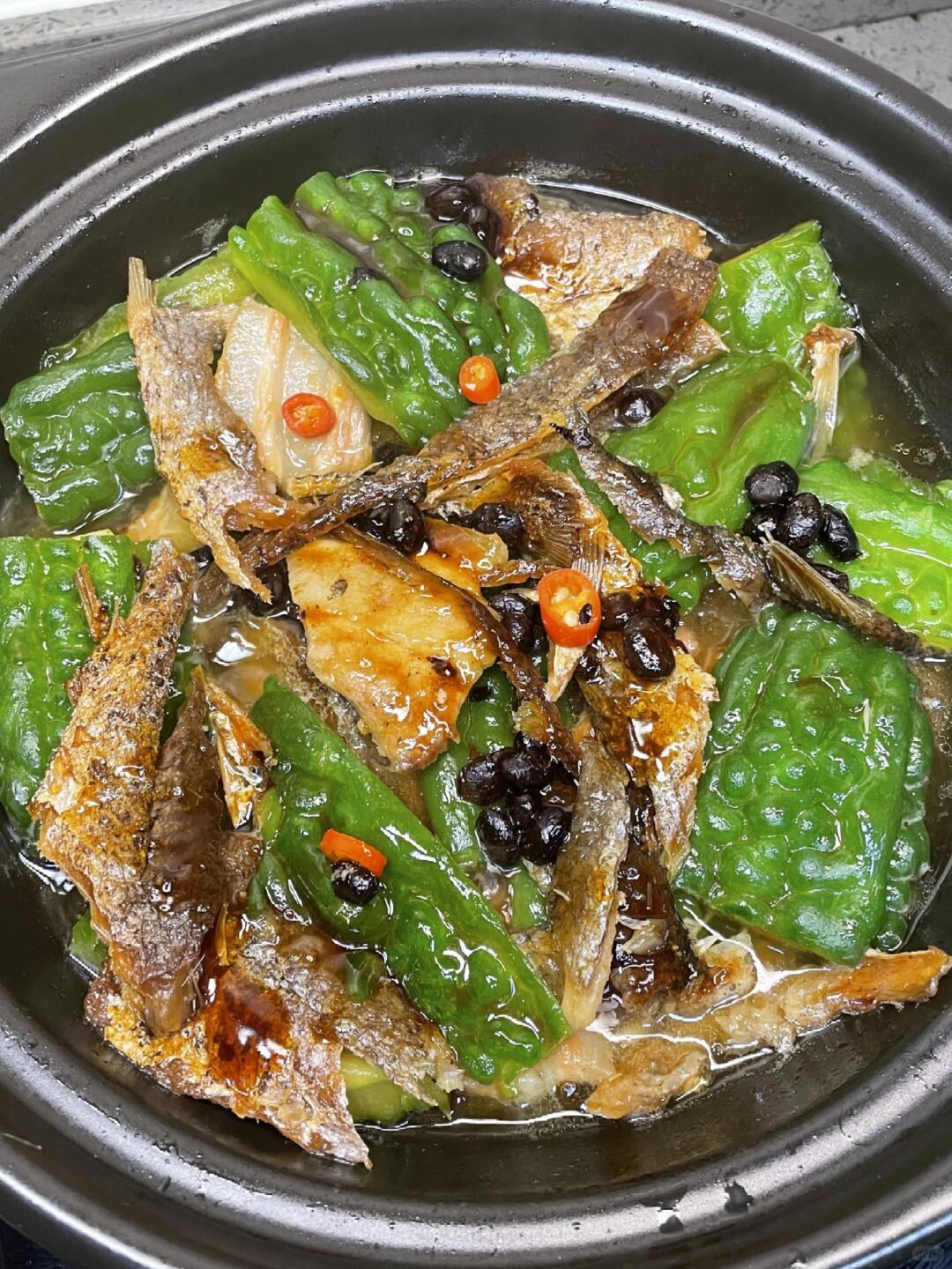 Ridged bitter melon pieces and brown fish pieces with black beans in a black clay pot.