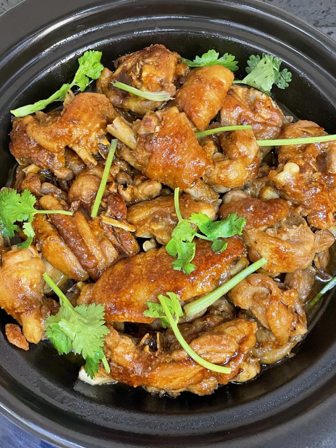 Browned chicken pieces with garlic and cilantro in a black clay pot.