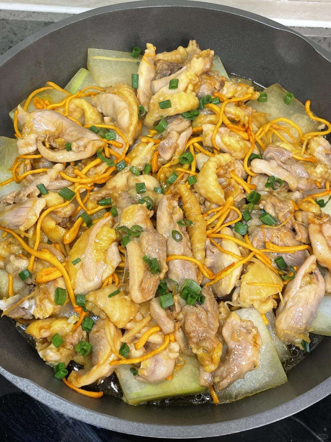 Chicken pieces, pale winter melon and orange cordyceps flowers in a dark pan.
