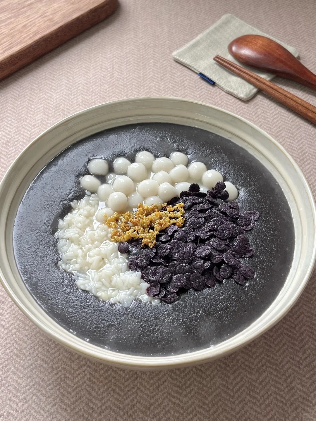 Dark sesame dessert topped with white rice balls and dark rice crisps.