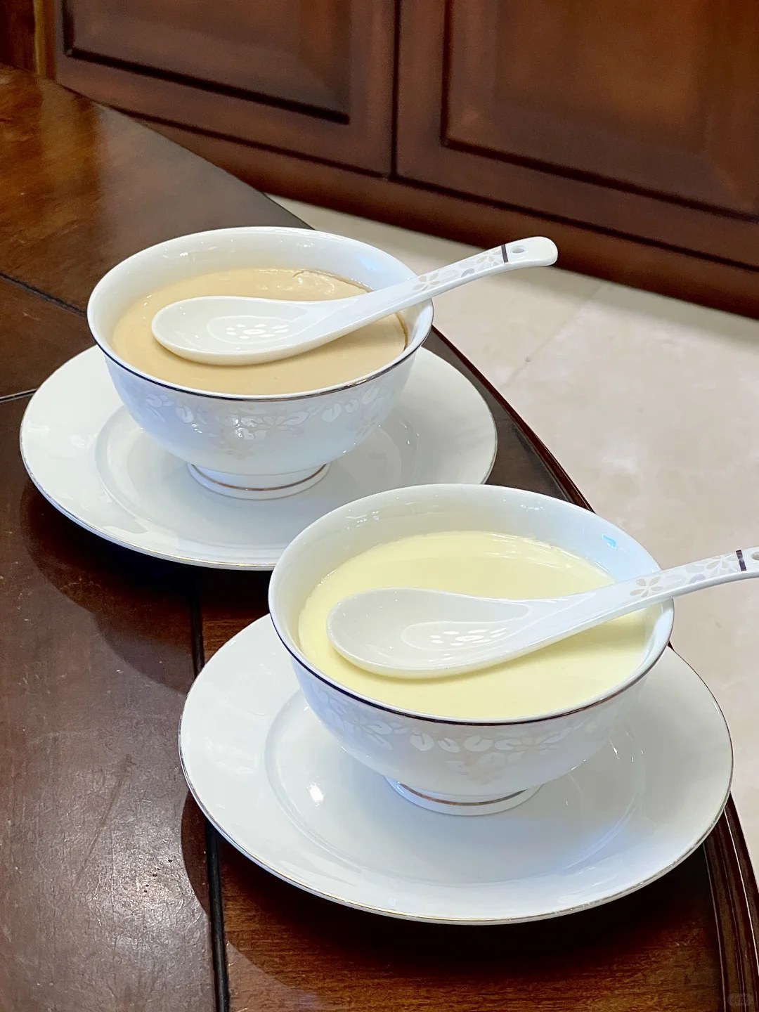 Two pale milk puddings in small white bowls with spoons.