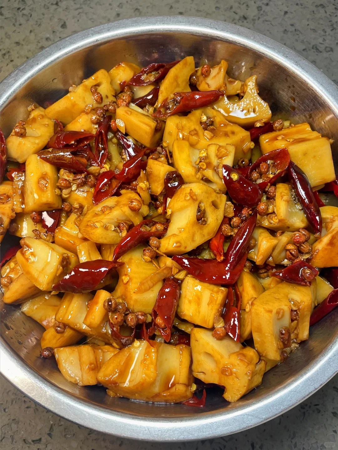 Lotus root cubes with dried red chiles, sesame-like seeds and green herbs in a metal bowl.