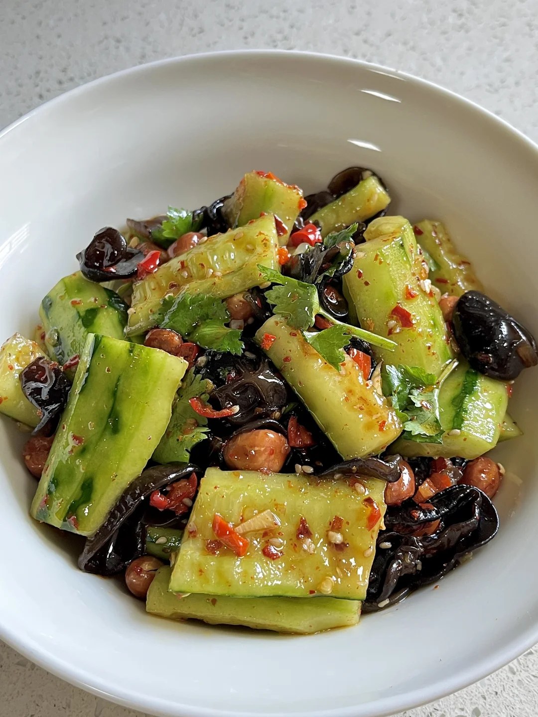 Green cucumber chunks and dark wood ear mushrooms topped with herbs and peanuts on a white plate.