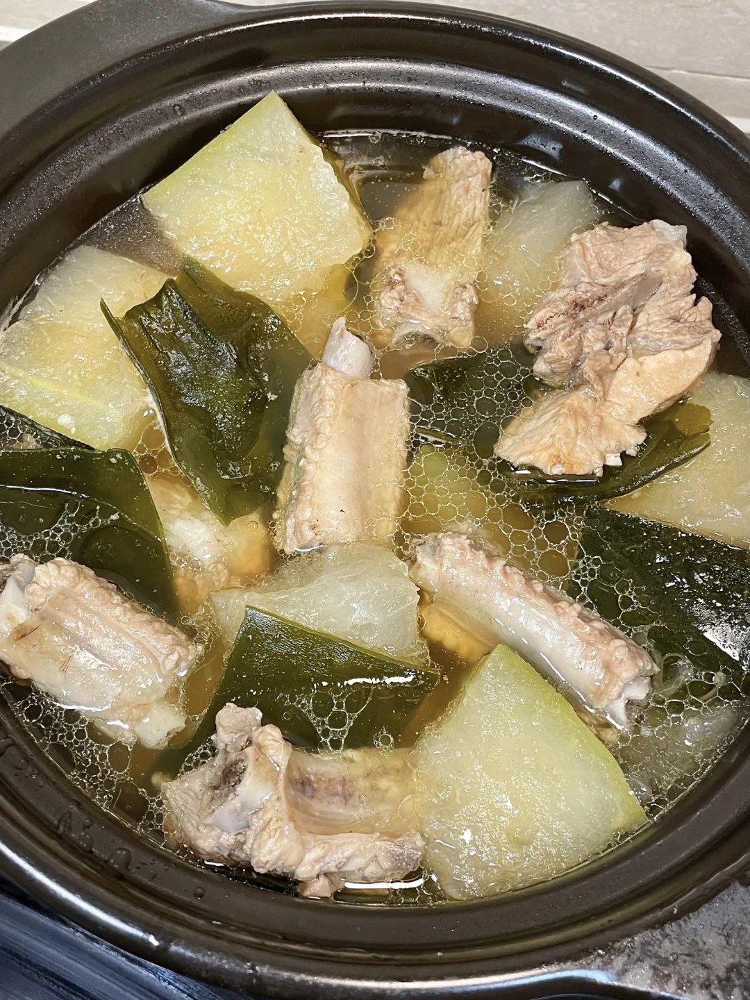 Pork ribs, pale winter melon and dark kelp in a black clay pot of clear soup.