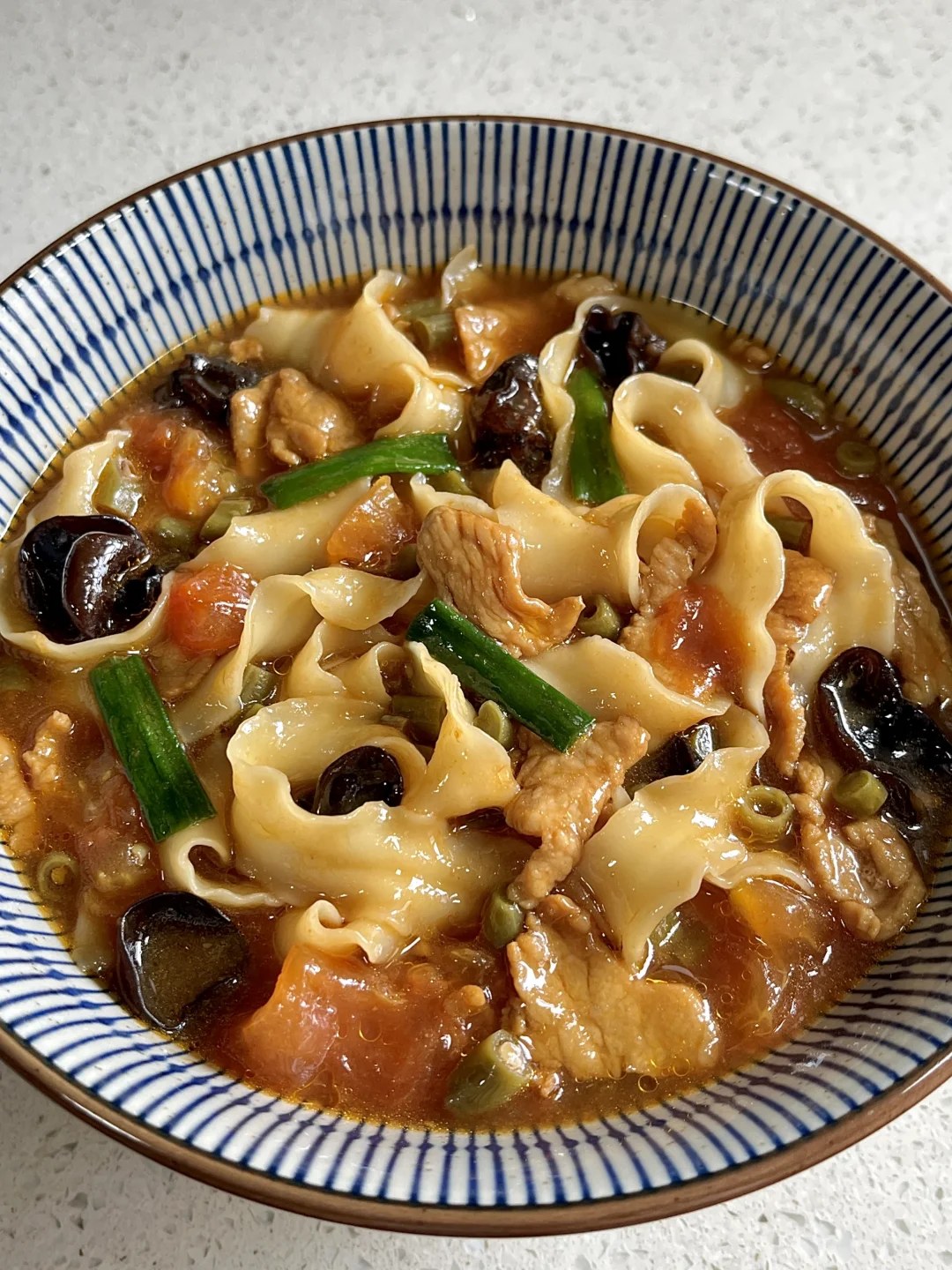 Broad curled noodles with meat and scallions in a striped soup bowl.