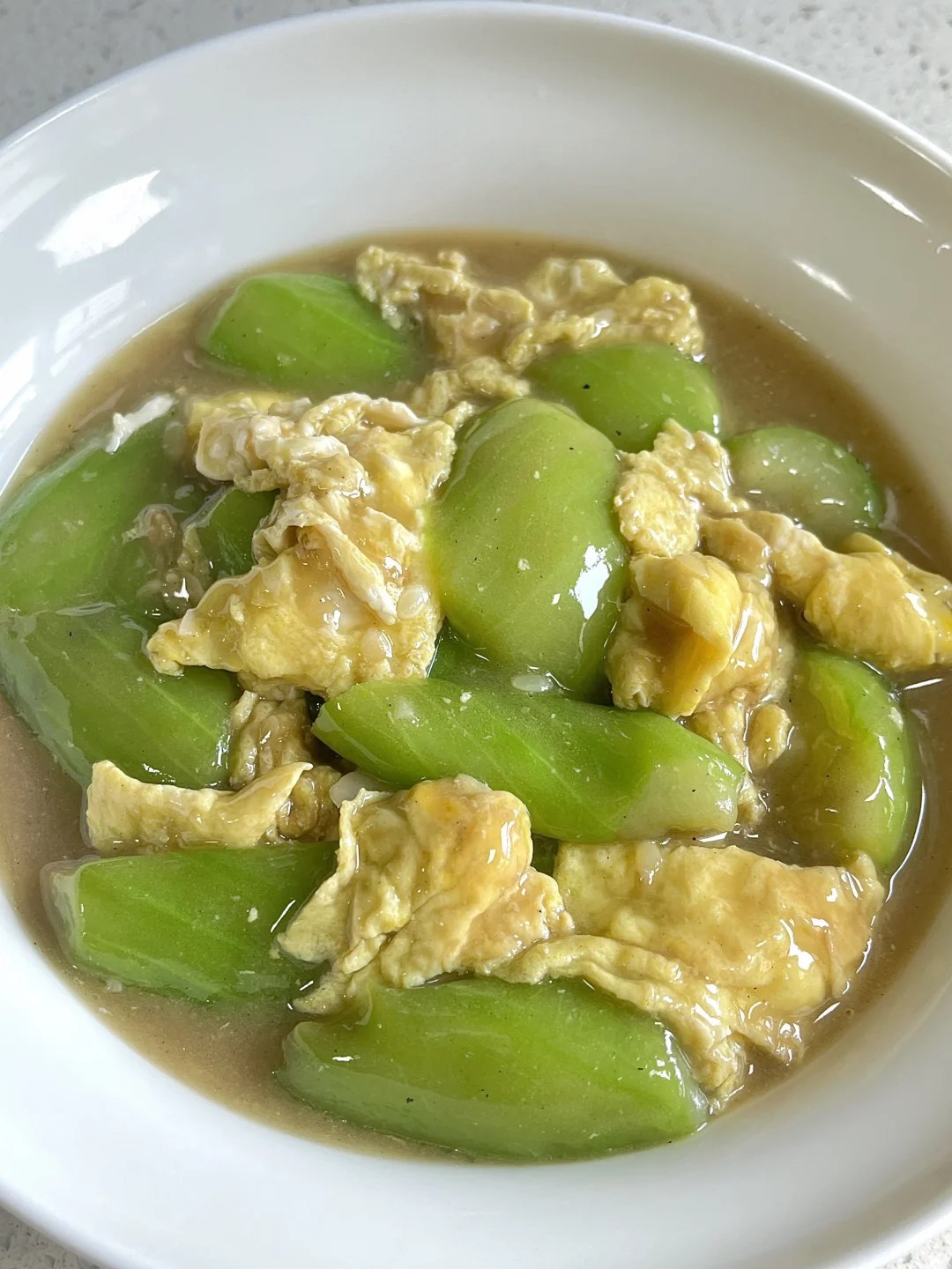 Pale-green luffa chunks and soft egg pieces in a shallow white bowl.