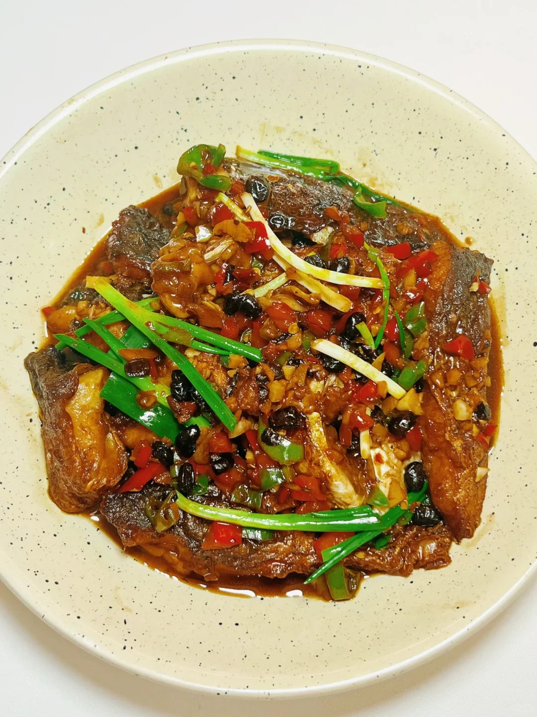 Brown fish chunks with sliced green and red peppers and scallion sections.