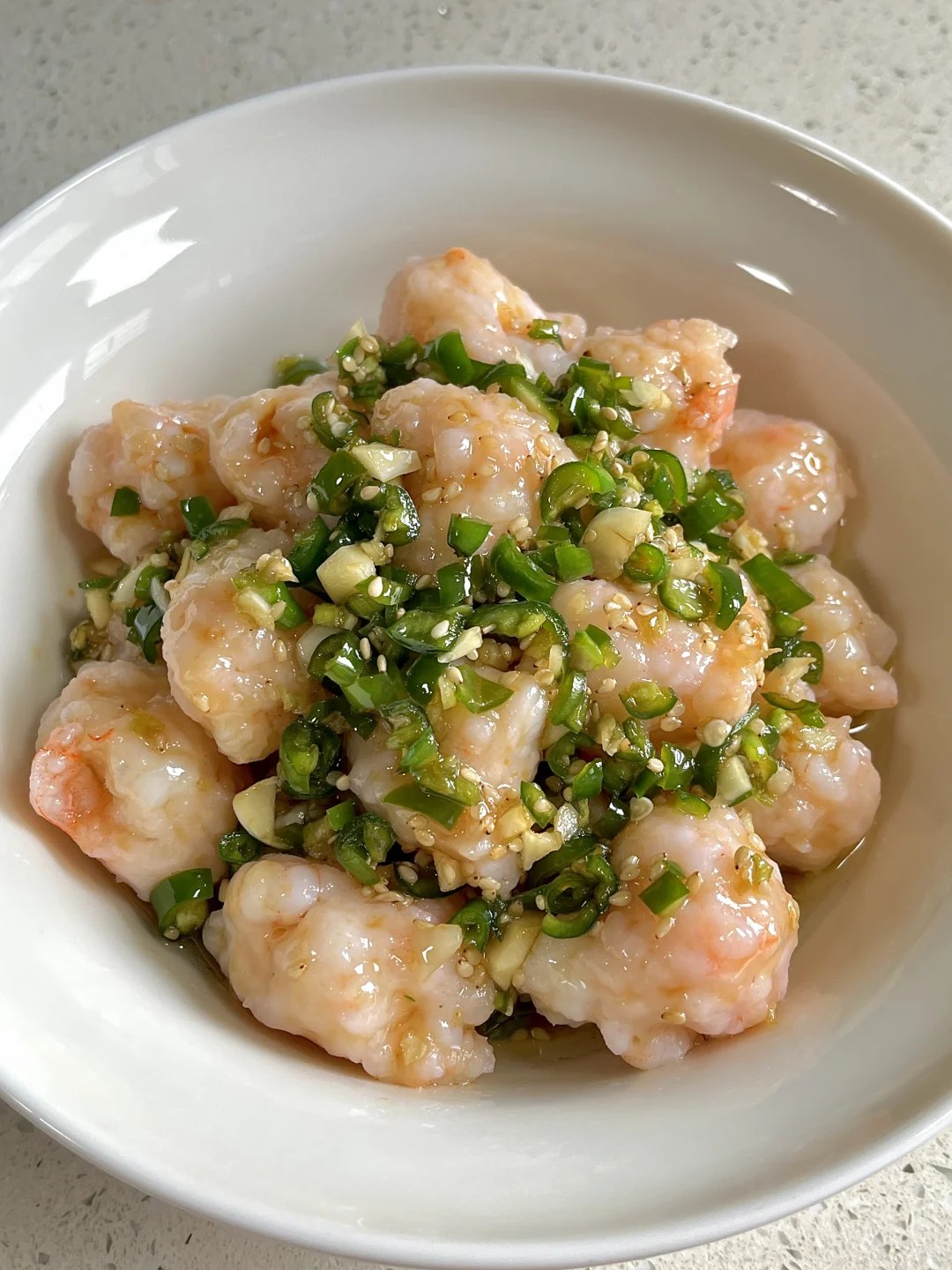 Pale shrimp dumplings topped with chopped green peppers and sesame in a white bowl.