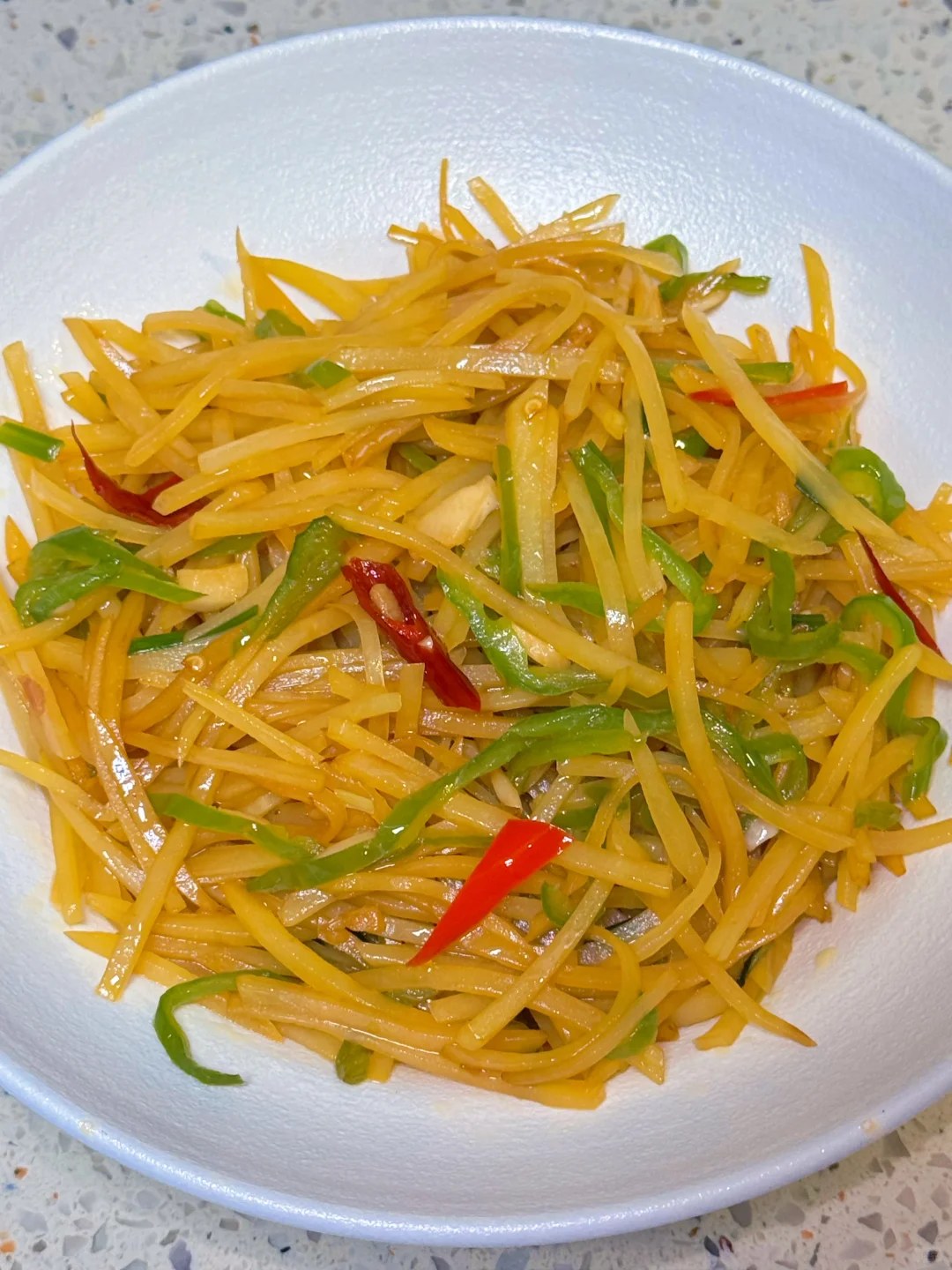 Fine yellow potato shreds with green pepper and red chile pieces.
