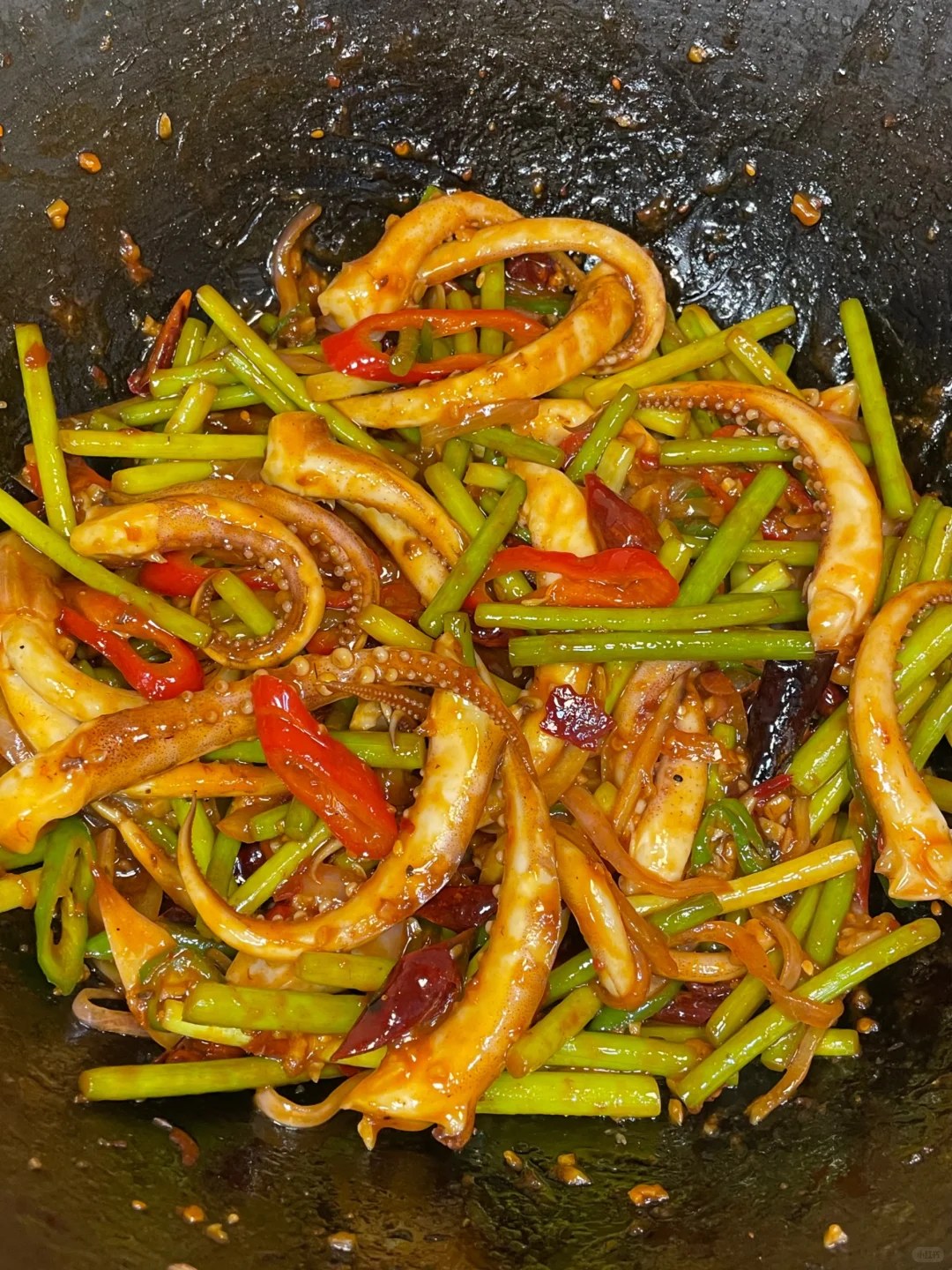 Squid tentacles and green garlic scapes with red peppers in a dark pan.