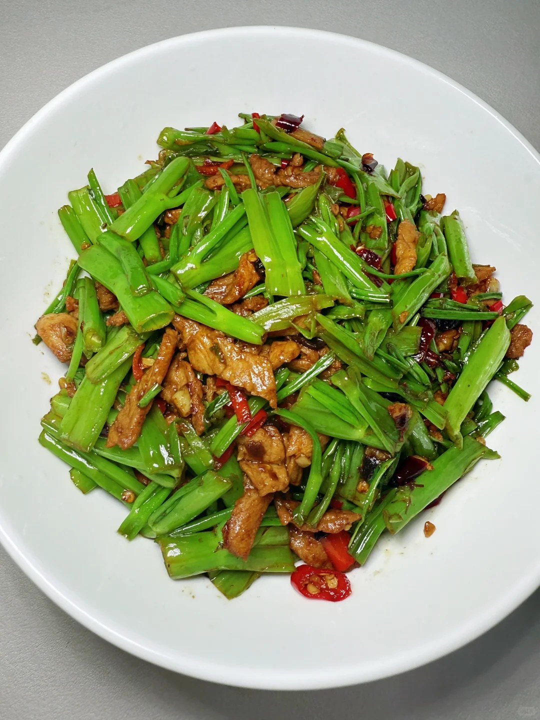 Green water spinach stems with thin meat strips and red chile pieces.