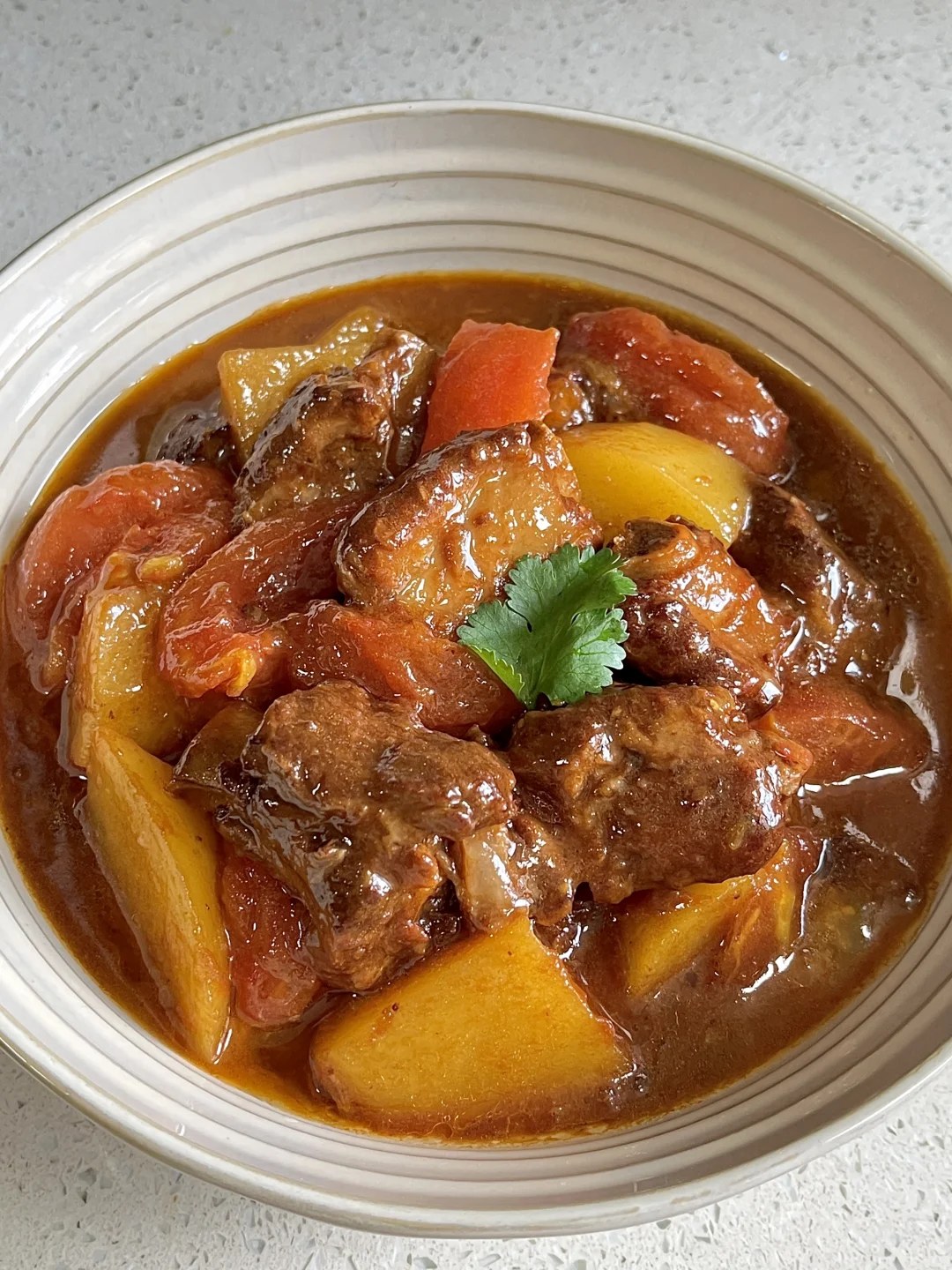 Pork ribs and potato chunks coated in red-brown tomato sauce in a striped bowl.
