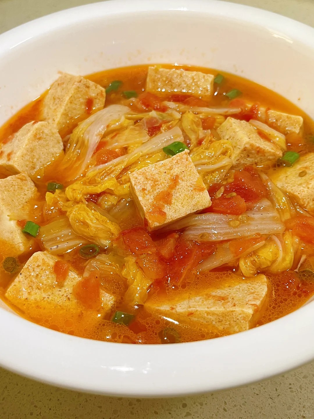 Pale tofu blocks and cabbage strips in an orange tomato broth.