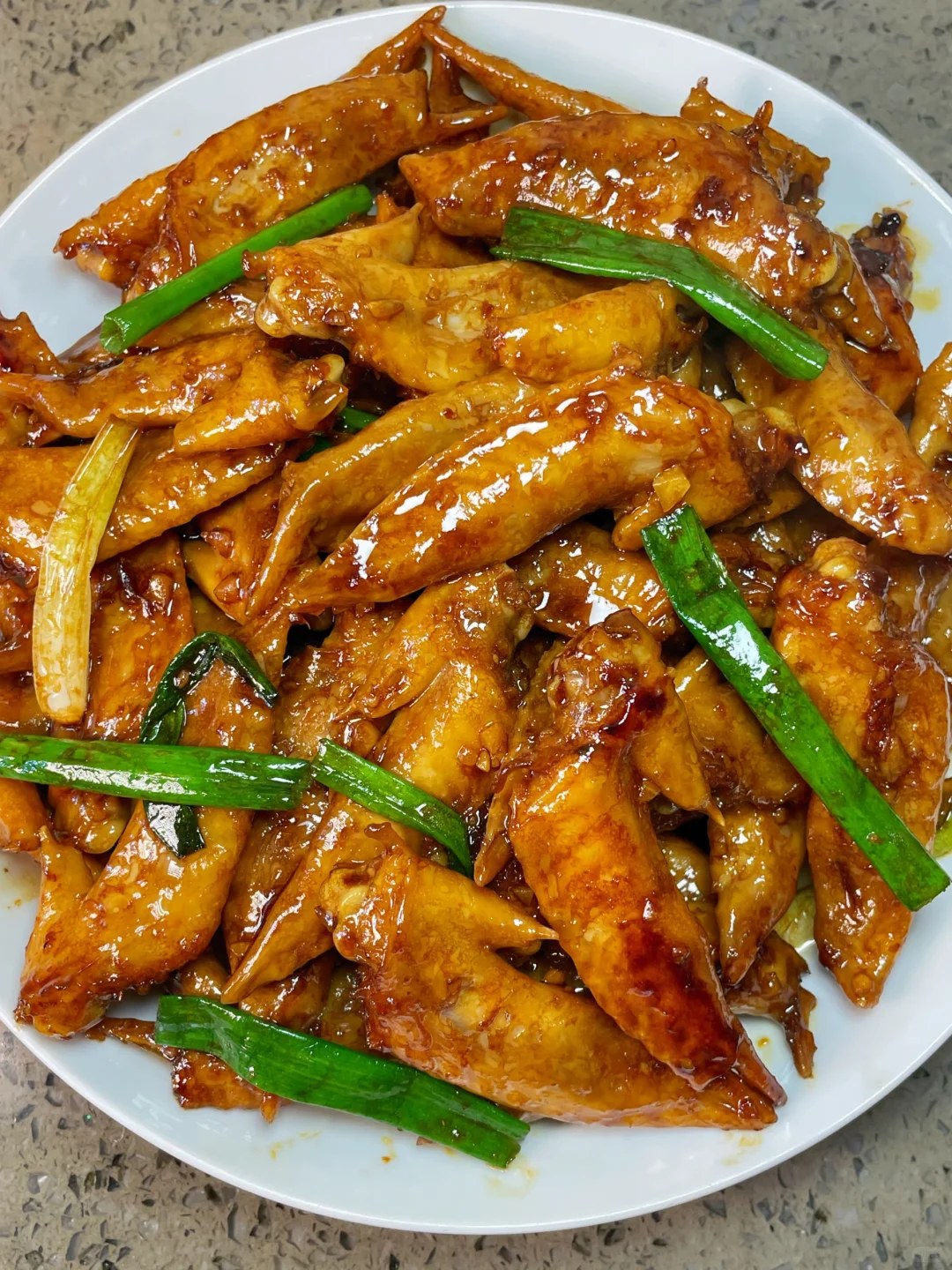 Glazed narrow chicken wing tips with green scallion sections on a white plate.