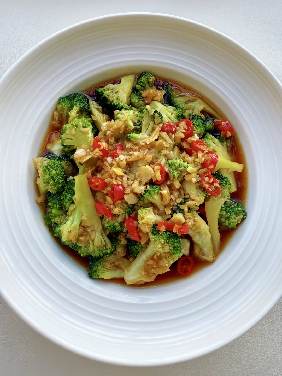 Green broccoli florets covered with garlic and small red chile pieces.