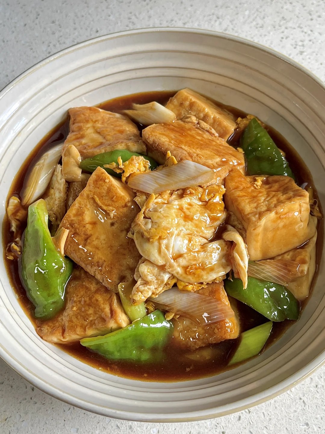 Golden tofu pieces, eggs, green pepper and large scallion sections in a striped bowl.