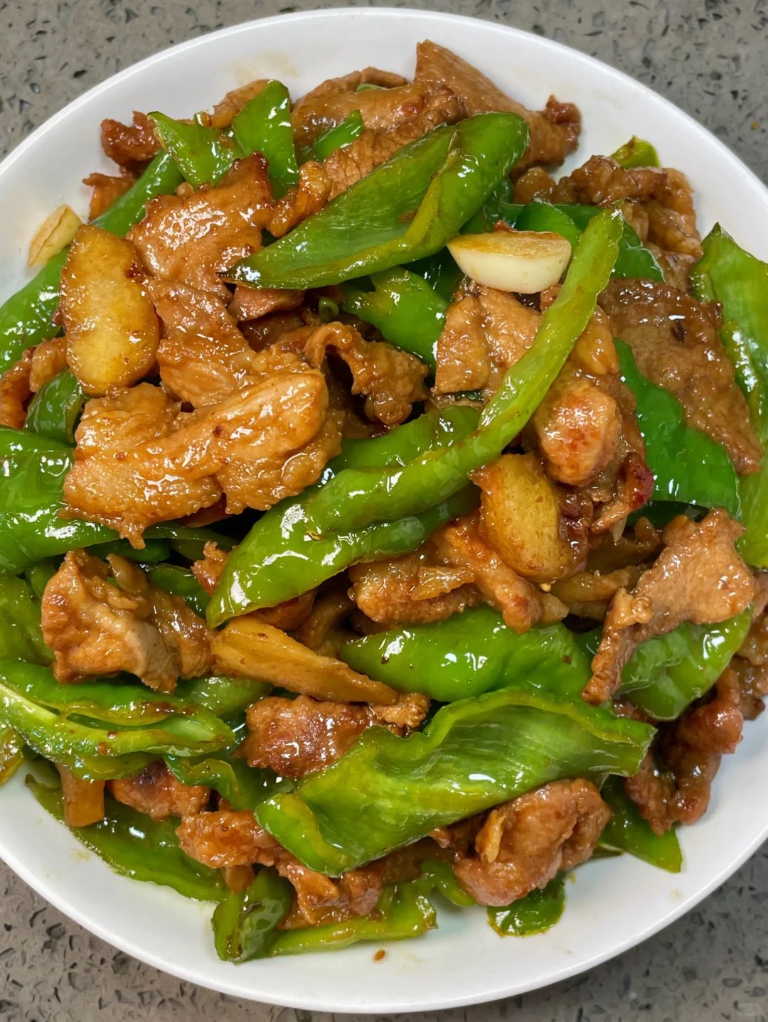 Brown pork pieces and bright green pepper sections on a white plate.