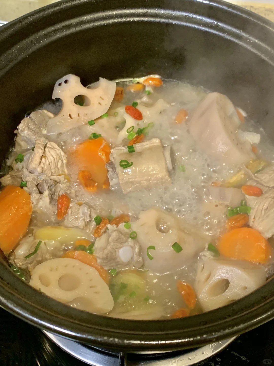 Pork ribs, lotus root slices and orange carrot pieces in a pale broth.