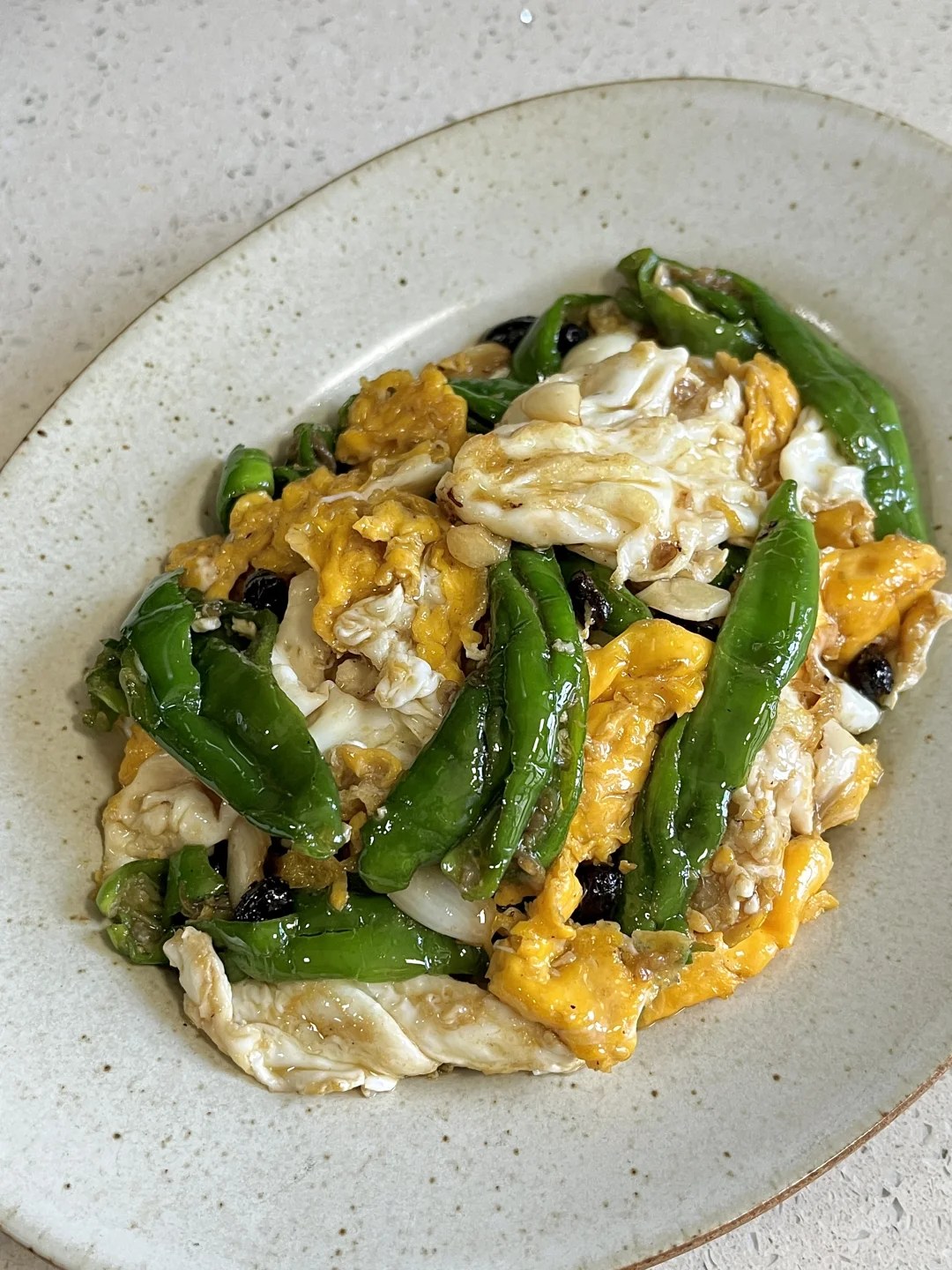 Soft egg pieces, broad green pepper pieces and dark black beans in a white bowl.